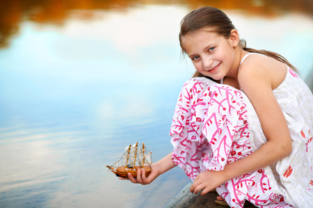 girl child playing with a toy sailing ship by the riverの写真素材