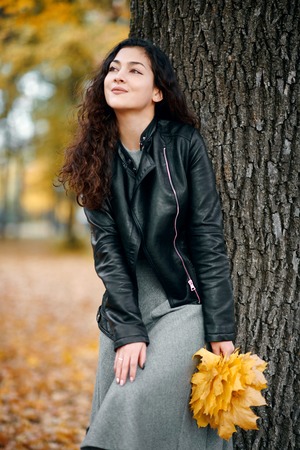 Woman with yellow leaves stand near big tree in autumn city park.の写真素材