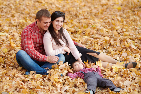 Parents and child are sitting in autumn city park. Bright yellow trees.の写真素材