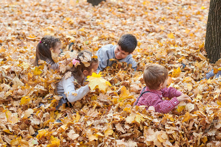 Children are lying and playing on fallen leaves in autumn city park.の写真素材