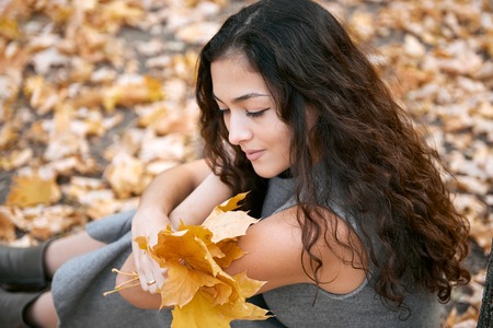 Pretty woman is sitting in autumn park near big tree.