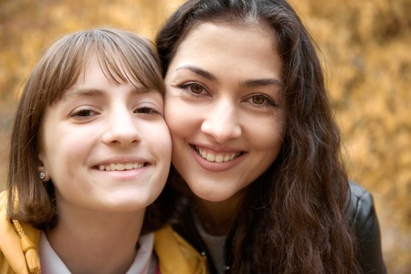 Portrait of pretty woman and teen girl. They are posing in autumn park. Beautiful landscape at fall...