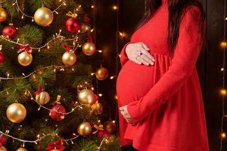 pregnant woman posing in christmas lights, red dress, holiday conceptの写真素材