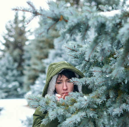 Sad woman is touching fir tree branches in winter forest