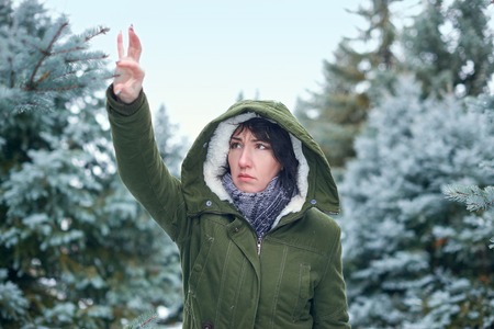 Sad woman is touching fir tree branches in winter forestの写真素材