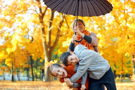 Happy family posing under umbrella, playing and having fun in autumn city park. Children and parents together having a nice day. Bright sunlight and yellow leaves on trees, fall season.の写真素材