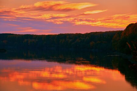 beautiful sunset in autumn season - trees silhouette near a river, bright sunlightの写真素材