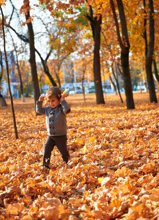 Happy child playing, posing, smiling and having fun in autumn city park. Bright yellow trees and leavesの写真素材