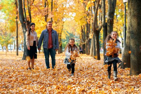 Happy family having holiday in autumn city park. Children and parents posing, smiling, playing and having fun. Bright yellow trees and leavesの写真素材