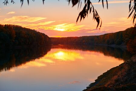 beautiful sunset in autumn season - trees silhouette near a river, bright sunlightの写真素材