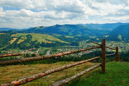 Village and spruces on hills - beautiful summer landscape, cloudy sky at bright sunny day. Carpathian mountains. Ukraine. Europe. Travel background.の写真素材
