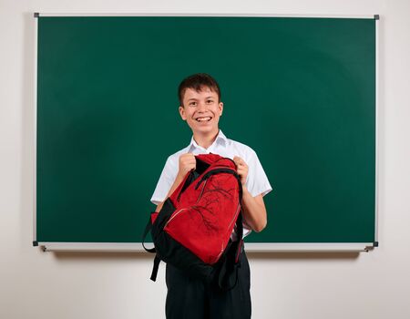 Portrait of a school boy looking for school supplies in his backpack, blackboard background - back to school and education conceptの写真素材