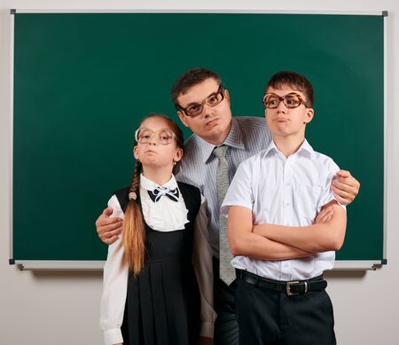 Portrait of a teacher, schoolboy and schoolgirl with old fashioned eyeglasses posing on blackboard background - back to school and education conceptの写真素材