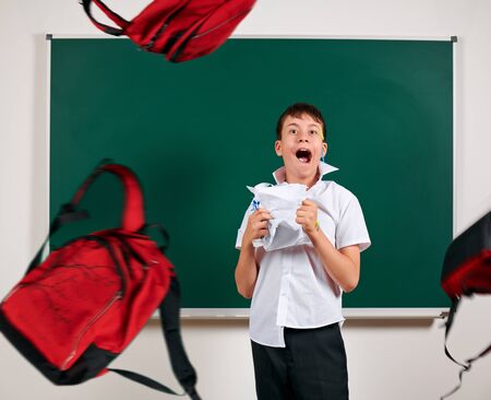 Portrait of funny pupil. School boy very emotional, having fun and very happy, blackboard background, flyuing backpacks - back to school and education conceptの写真素材