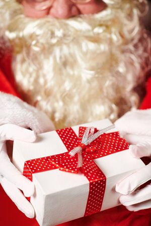 Closeup of Santa Claus hands with gift box, sitting indoor near decorated xmas tree with lights - Merry Christmas and Happy Holidays!の写真素材