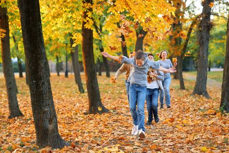 Happy family having holiday in autumn city park. Children and parents running, smiling, playing and having fun. Bright yellow trees and leavesの写真素材