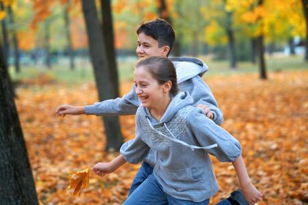 Girl and boy teenager having holiday in autumn city park, running, smiling, playing and having fun. Bright yellow trees and leavesの写真素材