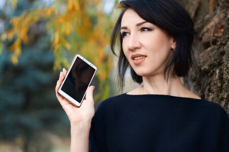 Beautiful elegant woman talking by phone and posing in a city park in autumnの写真素材