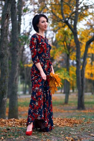 Beautiful elegant woman standing and posing with bouquet of yellow leaves in autumn city parkの写真素材