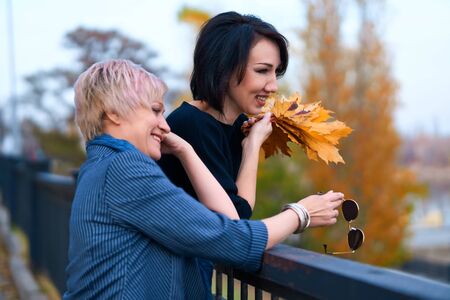 Two girlfriends talking and posing in autumn city park. Beautiful adult woman, blond and brunette.の写真素材