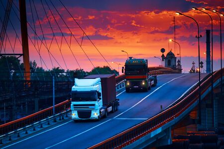 truck with container rides over the bridge, beautiful sunset, freight cars in industrial seaport, the road goes upの写真素材