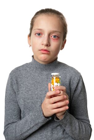 Allergic reaction, skin rash, close view portrait of a girl's face. Redness and inflammation of the skin in the eyes and lips. Immune system disease. Bottle of tablets and pills in child hand.の写真素材