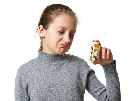 Allergic reaction, skin rash, close view portrait of a girl's face. Redness and inflammation of the skin in the eyes and lips. Immune system disease. Bottle of tablets and pills in child hand.の写真素材