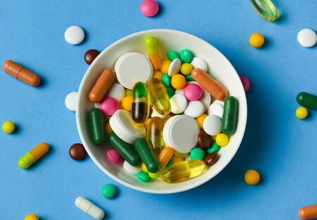 A dish full of pills, tablets, vitamins, drugs, omega 3 fish oil, gel capsules, medicament and food supplement for health care. Blue background.の写真素材
