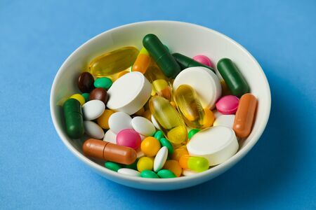 A dish full of pills, tablets, vitamins, drugs, omega 3 fish oil, gel capsules, medicament and food supplement for health care. Blue background.の写真素材