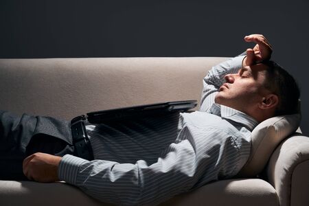 businessman is lying on the sofa with laptop and restingの写真素材