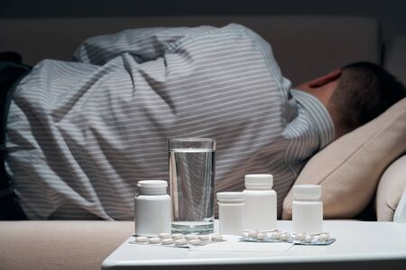 Overworked businessman is lying on the sofa and resting. Pills and glass of water near him.の写真素材