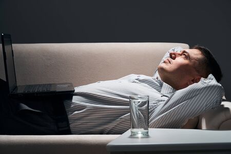 businessman is lying on the sofa with laptop and resting