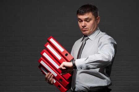 Very busy businessman closeup portrait, posing with red folders, overworking concept, dark wall...