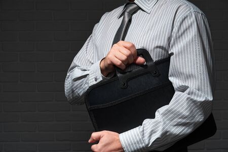Businessman closeup portrait, he standing and posing with briefcase, dark wall backgroundの写真素材