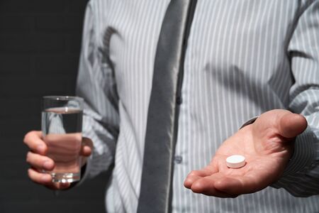 Businessman closeup portrait, he standing and posing with pills, health and medication concept, dark wall backgroundの写真素材