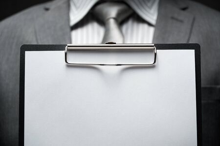 white blank paper sheet closeup in businessman hand, gray suit, dark wall background, blank space for textの写真素材