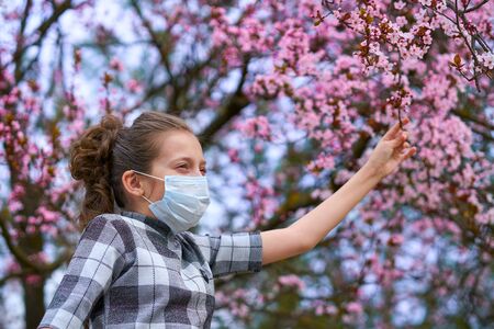 girl with a face mask is in the city outdoor, blooming trees, spring season, flowering time - concept of allergies and health protection from dusty airの写真素材