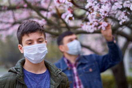father and son with a face mask are in the city outdoor, blooming trees, spring season, flowering time - concept of allergies and health protection from dusty airの写真素材