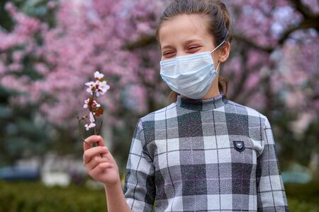 girl with a face mask is in the city outdoor, blooming trees, spring season, flowering time - concept of allergies and health protection from dusty airの写真素材