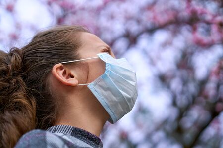 girl with a face mask is in the city outdoor, blooming trees, spring season, flowering time - concept of allergies and health protection from dusty airの写真素材