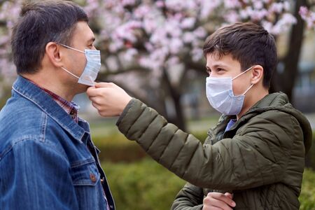 father and son with a face mask are in the city outdoor, blooming trees, spring season, flowering time - concept of allergies and health protection from dusty airの写真素材