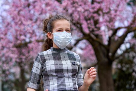 girl with a face mask is in the city outdoor, blooming trees, spring season, flowering time - concept of allergies and health protection from dusty airの写真素材