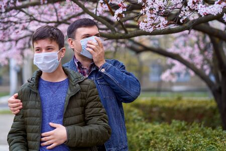 father and son with a face mask are in the city outdoor, blooming trees, spring season, flowering...