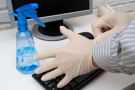 concept of cleaning or disinfecting the office - a businessman cleans the workplace, computer, desk, uses a spray gun and paper napkins. Cleaning surfaces from microbes, viruses and dirt.の写真素材