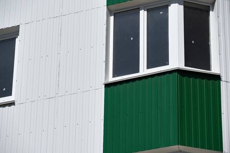 facade of a new multistory building with white and green metal siding, many Windows