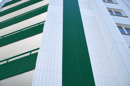 facade of a new multistory building with white and green metal siding, many Windows