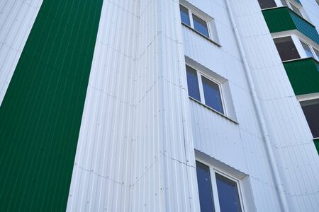 facade of a new multistory building with white and green metal siding, many Windows