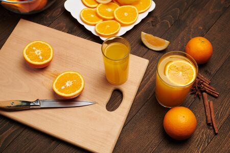 Fresh orange fruit whole and sliced on a wooden table, cutting board and kitchen knife. A plate full of citrus slices - natural and healthy food. Glass of fruit cocktail.の写真素材