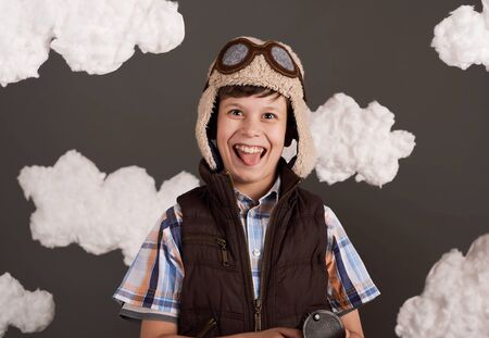 a boy dressed in a retro style jacket and helmet with glasses and dreams of becoming a pilot, clouds of cotton wool, gray background, tinted in brownの写真素材