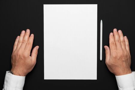 a blank sheet of paper and a businessman's hands on a black table, a white shirt and a wrist watch, a top view-a template for any text or inscriptionの写真素材